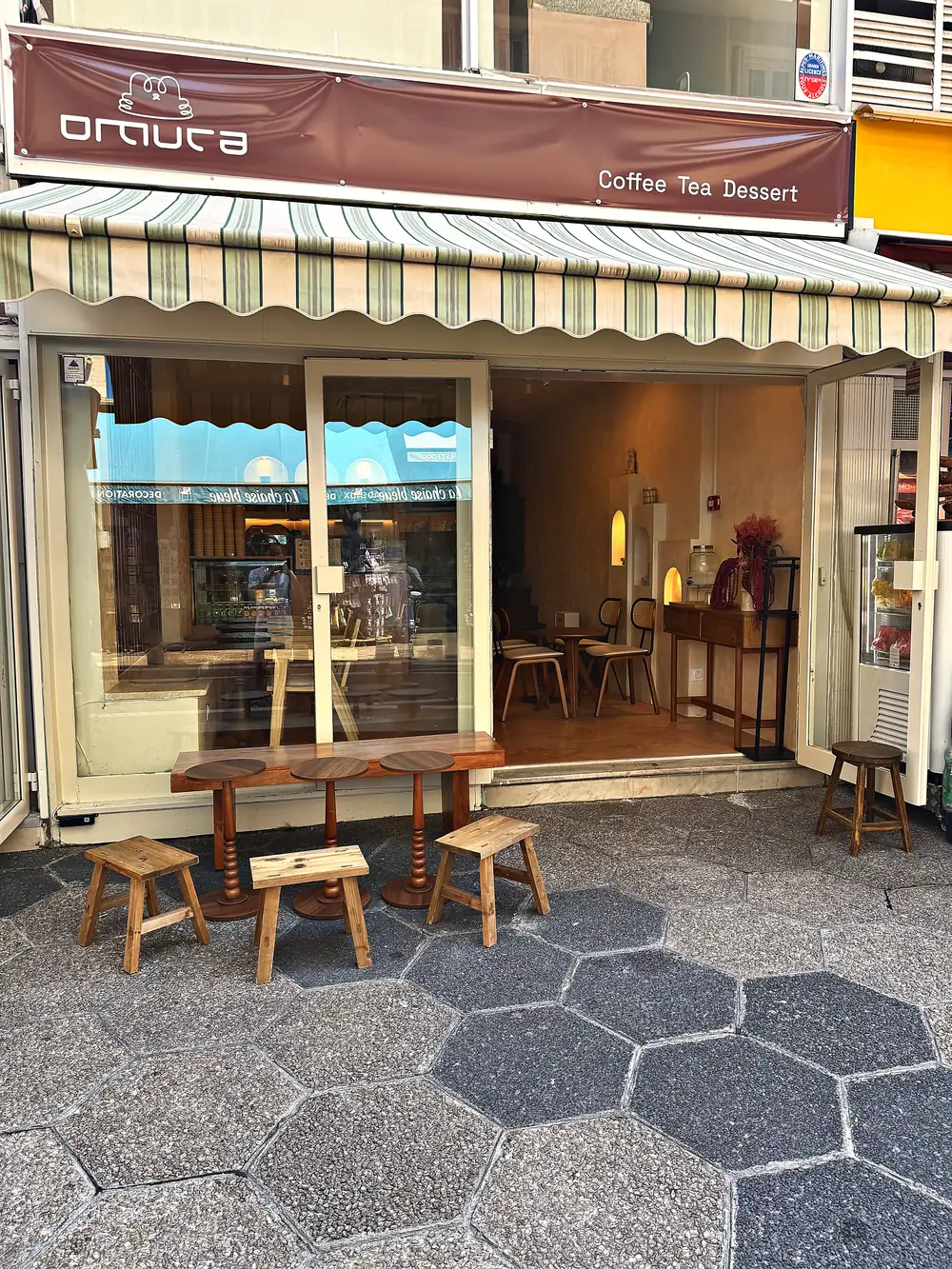 Devanture du coffee shop Omura au 2 rue Halévy à Nice : enseigne brune, store rayé vert, tabourets en bois sur le trottoir