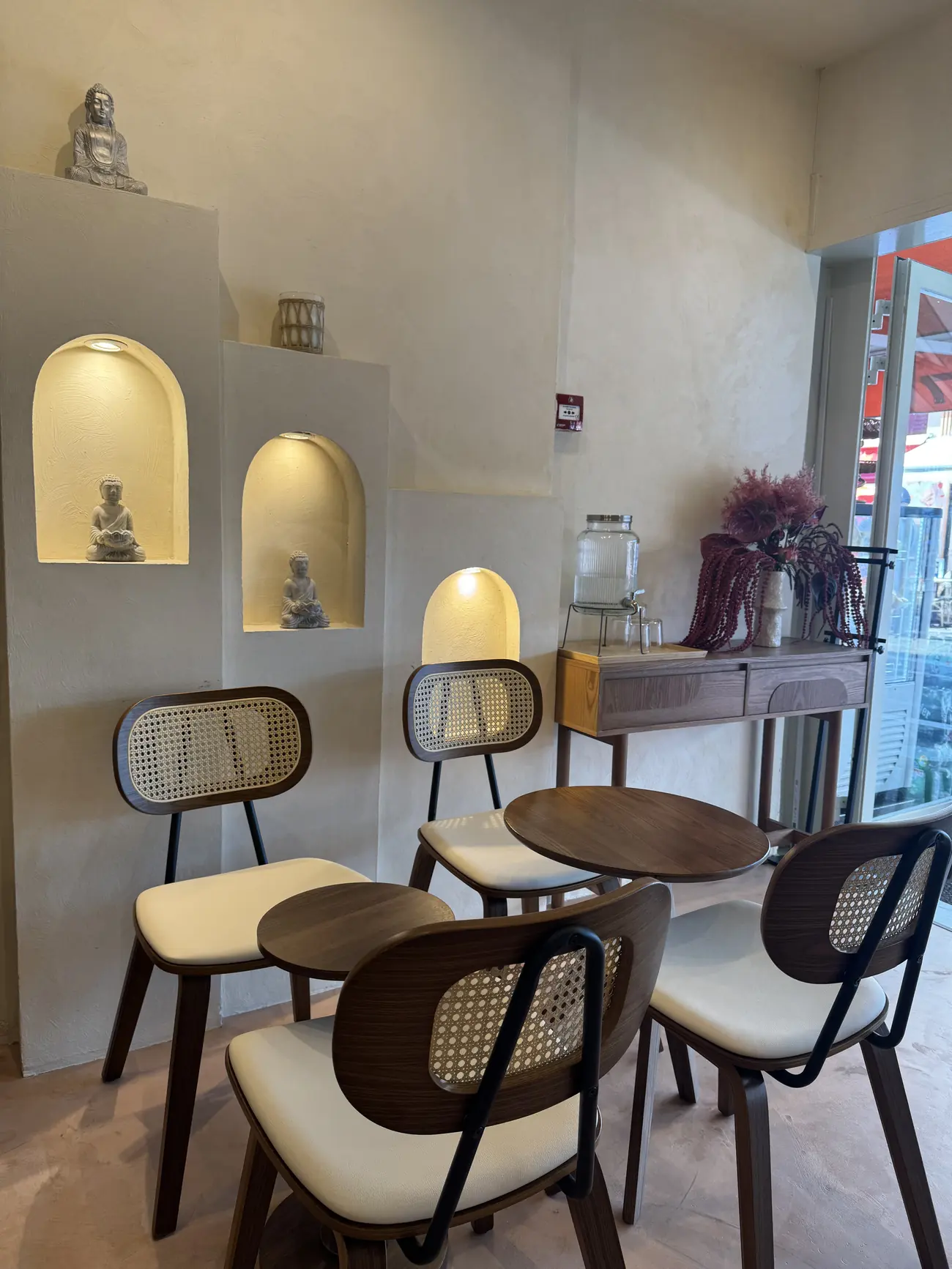 Salle du coffee shop Omura à Nice : murs en plâtre, niches voûtées éclairées, statues de Bouddha, chaises en cannage