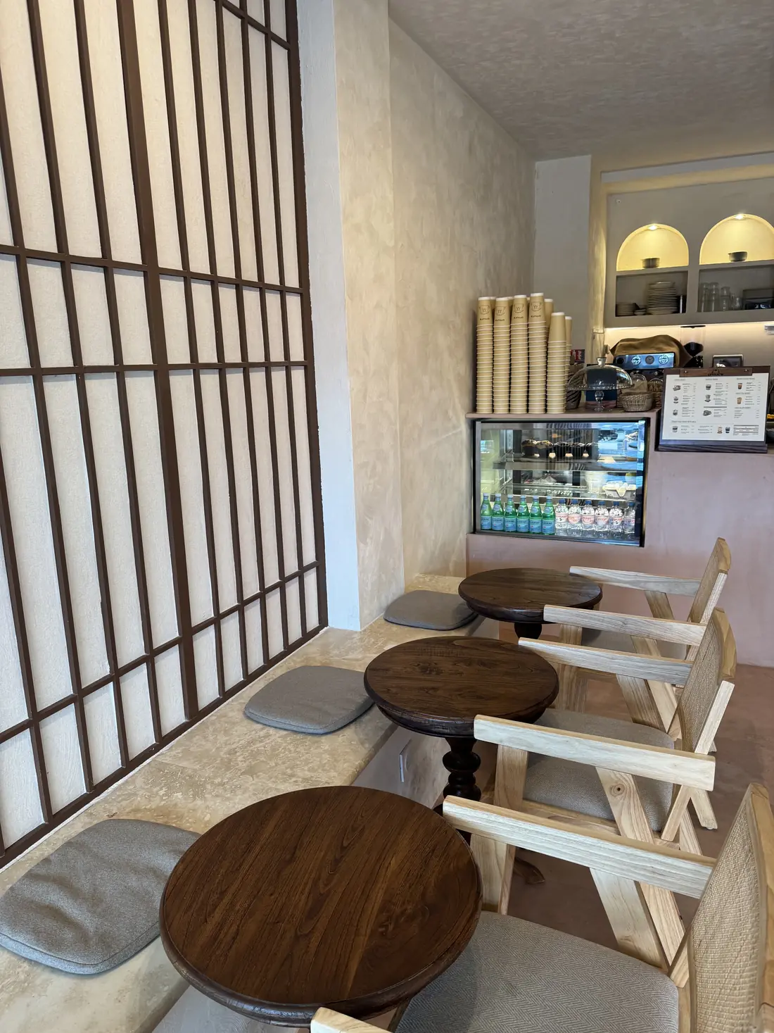 Intérieur d'Omura à Nice : cloison shoji en papier, banquette en travertin, tables rondes en bois et comptoir